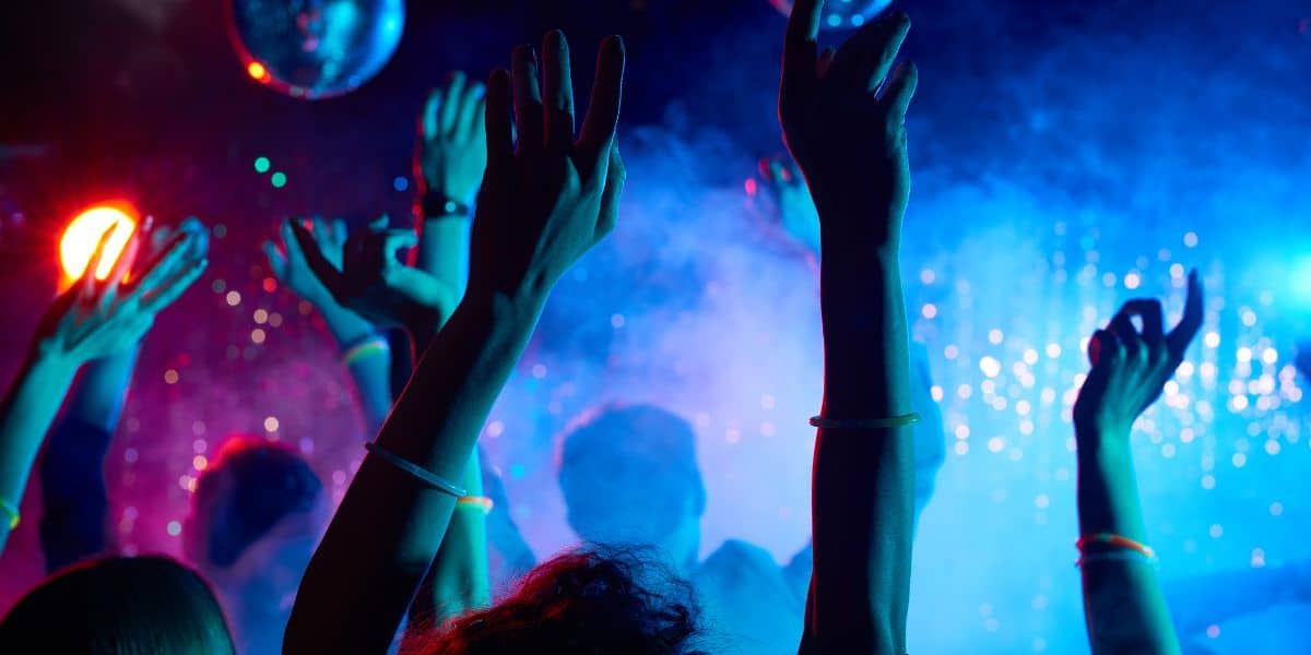 Energetic crowd enjoying the nightlife with hands raised under vibrant club lights and the glow of neon wristbands at one of the best gay bars in brighton.