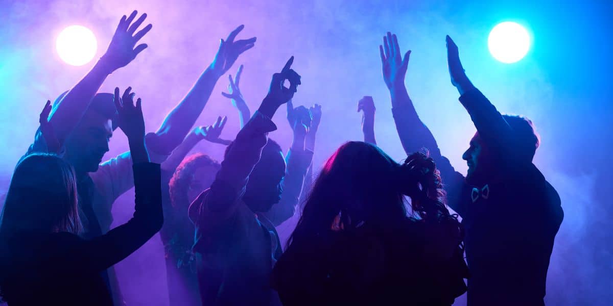 A group of people dancing and raising their hands in the air at one of the best gay clubs in london, illuminated by vibrant purple and blue lights.